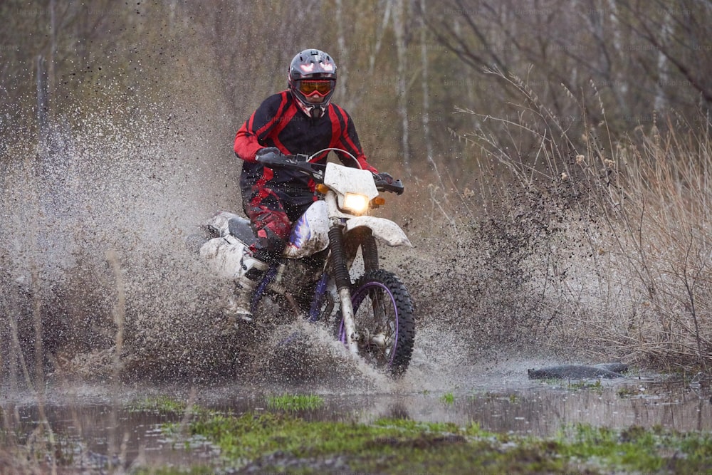 Motorcross rider racing in flooded wood down road with big puddles