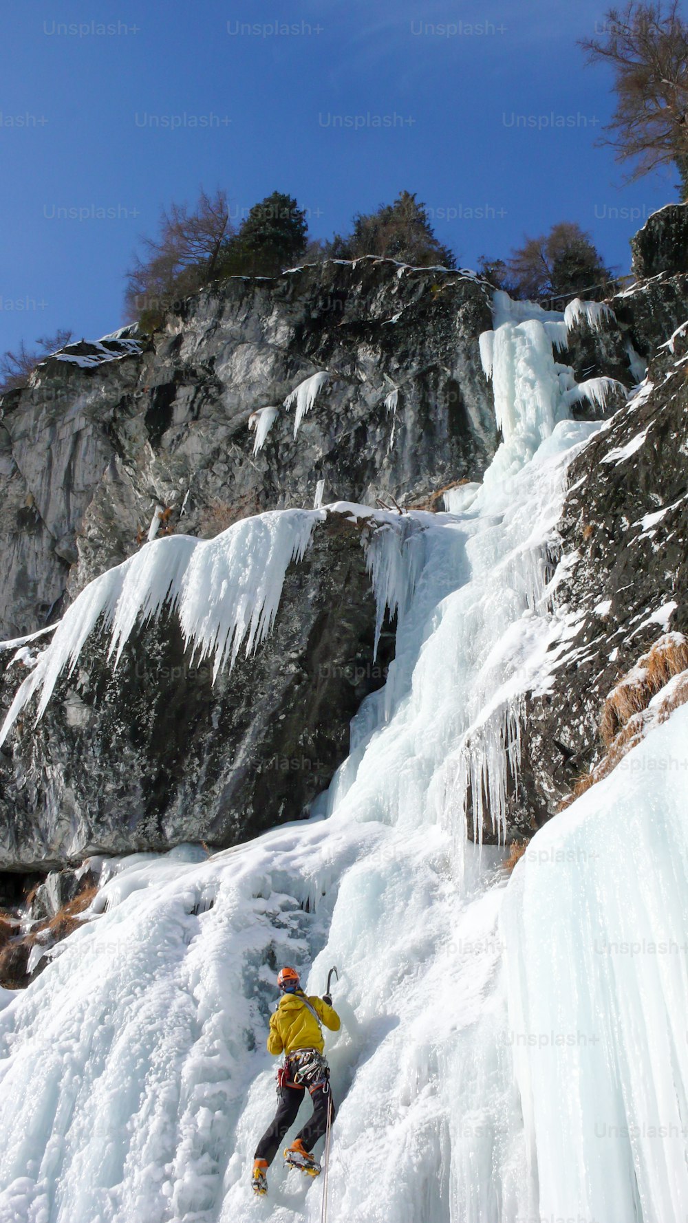 male mountain guide climbing a steep frozen waterfall on a cold winter day in the Alps