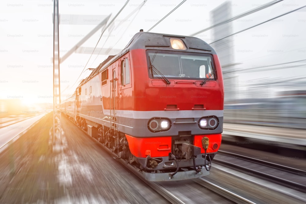 Treno passeggeri rosso ad alta velocità che sfreccia attraverso la ferrovia la sera al tramonto