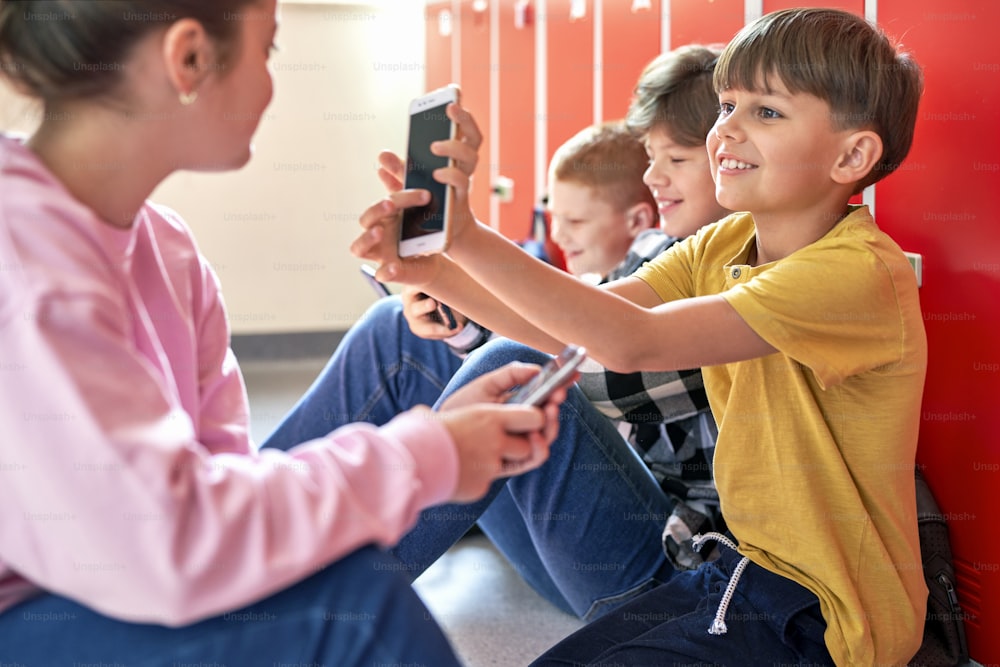 Niños en edad escolar sentados en el suelo y usando el teléfono inteligente