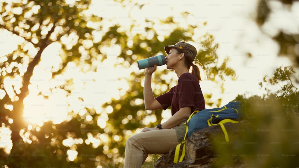 Junge Frau trinkt Wasser mit geschlossenen Augen, während sie eine Pause vom Wandern in der Natur macht.