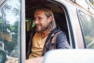 Handsome long haired bearded man looking away while riding at the car at the nature. Stock photo