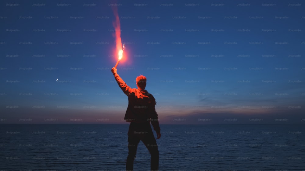 Der Mann mit einem Feuerstab steht auf dem Berggipfel in der Nähe des Meeres