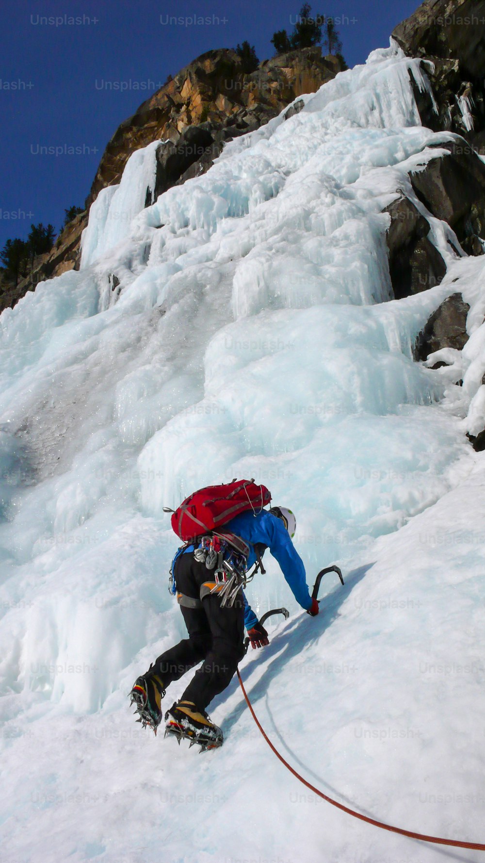 スイスの真冬のアルプスでゴージャスな凍った滝を登る青いジャケットを着た男性のアイスクライマー
