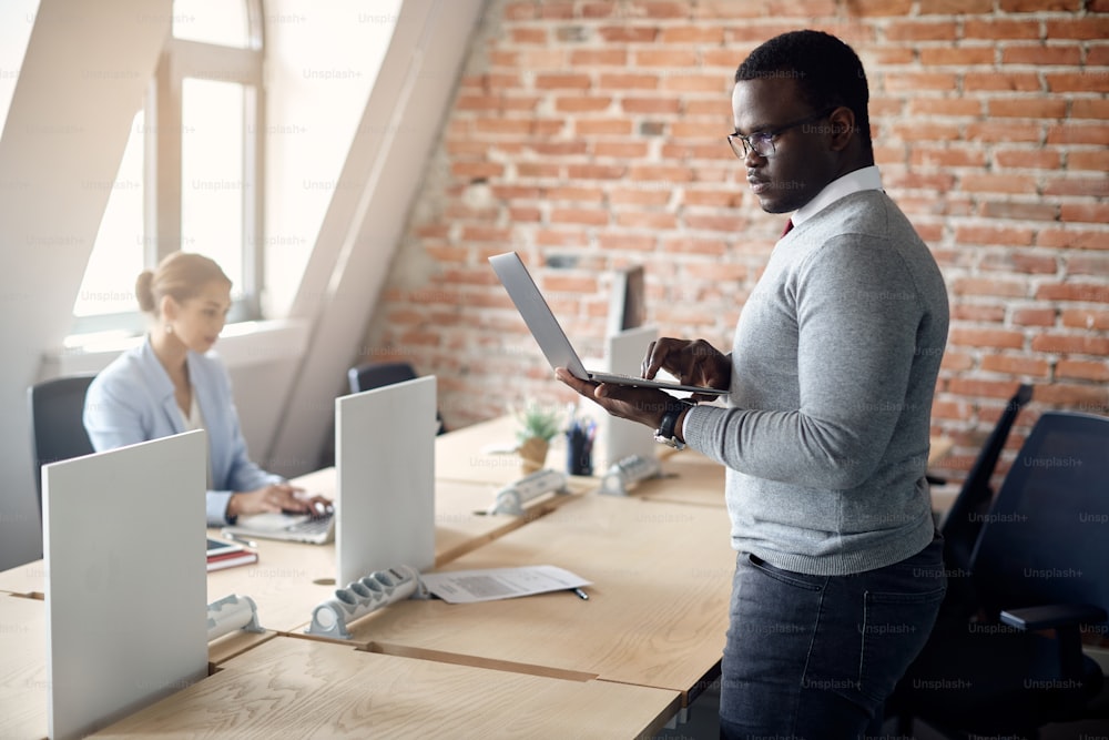 Hombre de negocios afroamericano leyendo un correo electrónico y trabajando en una computadora portátil en la oficina.