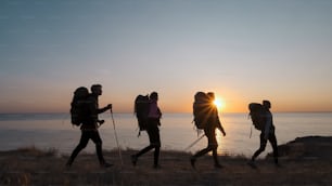 The four tourists with backpacks walking on the seascape background