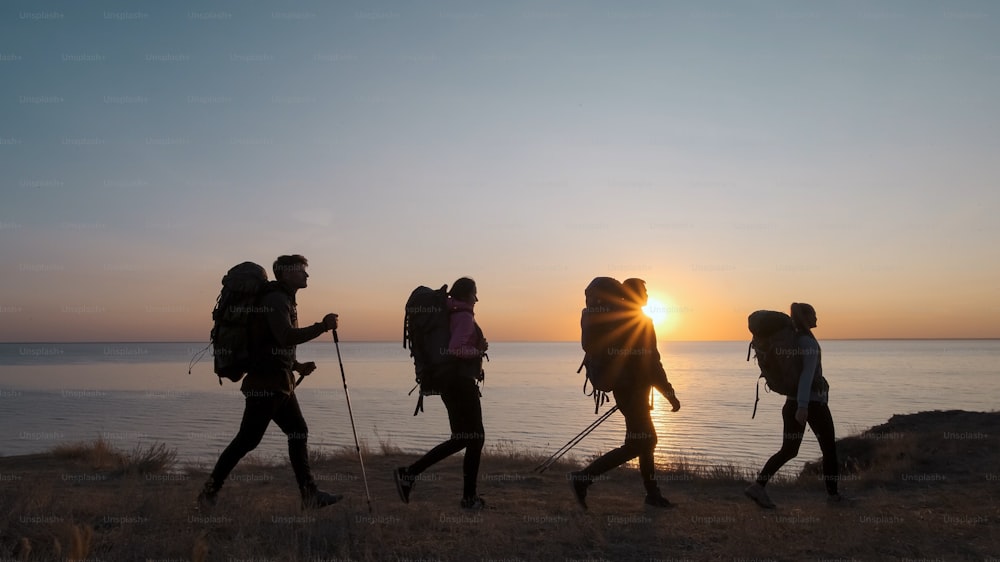 The four tourists with backpacks walking on the seascape background