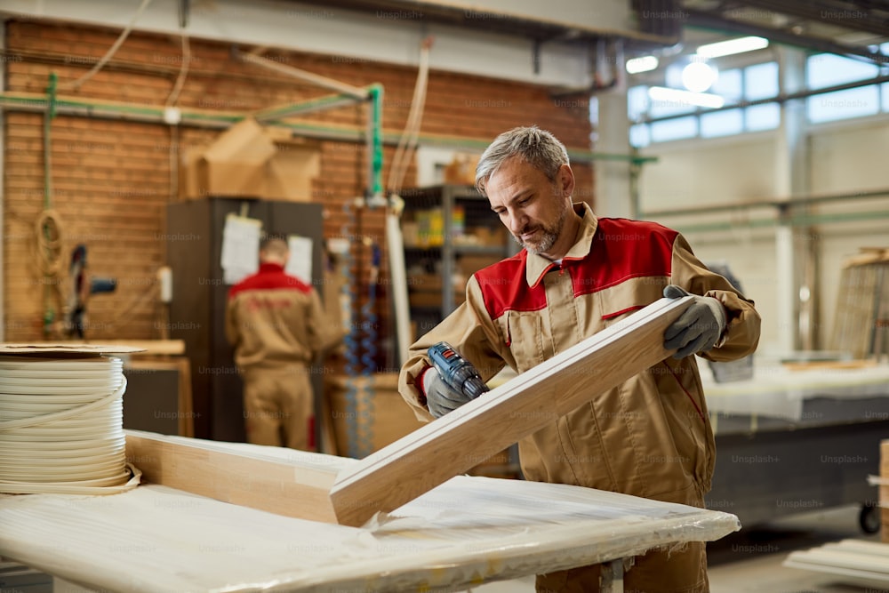 Ouvrier à l’aide d’une perceuse lors de la fabrication de meubles dans un atelier de menuiserie.