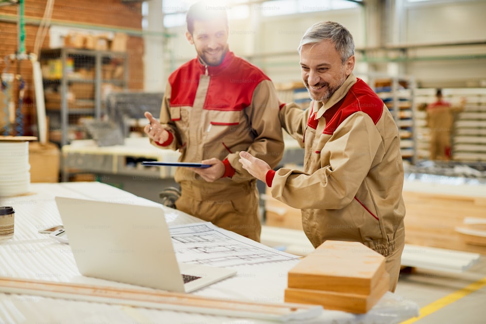 Trabajador feliz y sus colegas usando una computadora portátil durante una videollamada desde un taller de carpintería.