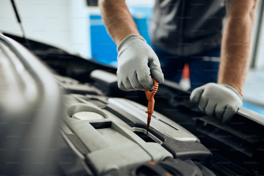 Gros plan d’un réparateur automobile vérifiant l’huile de voiture dans un atelier.