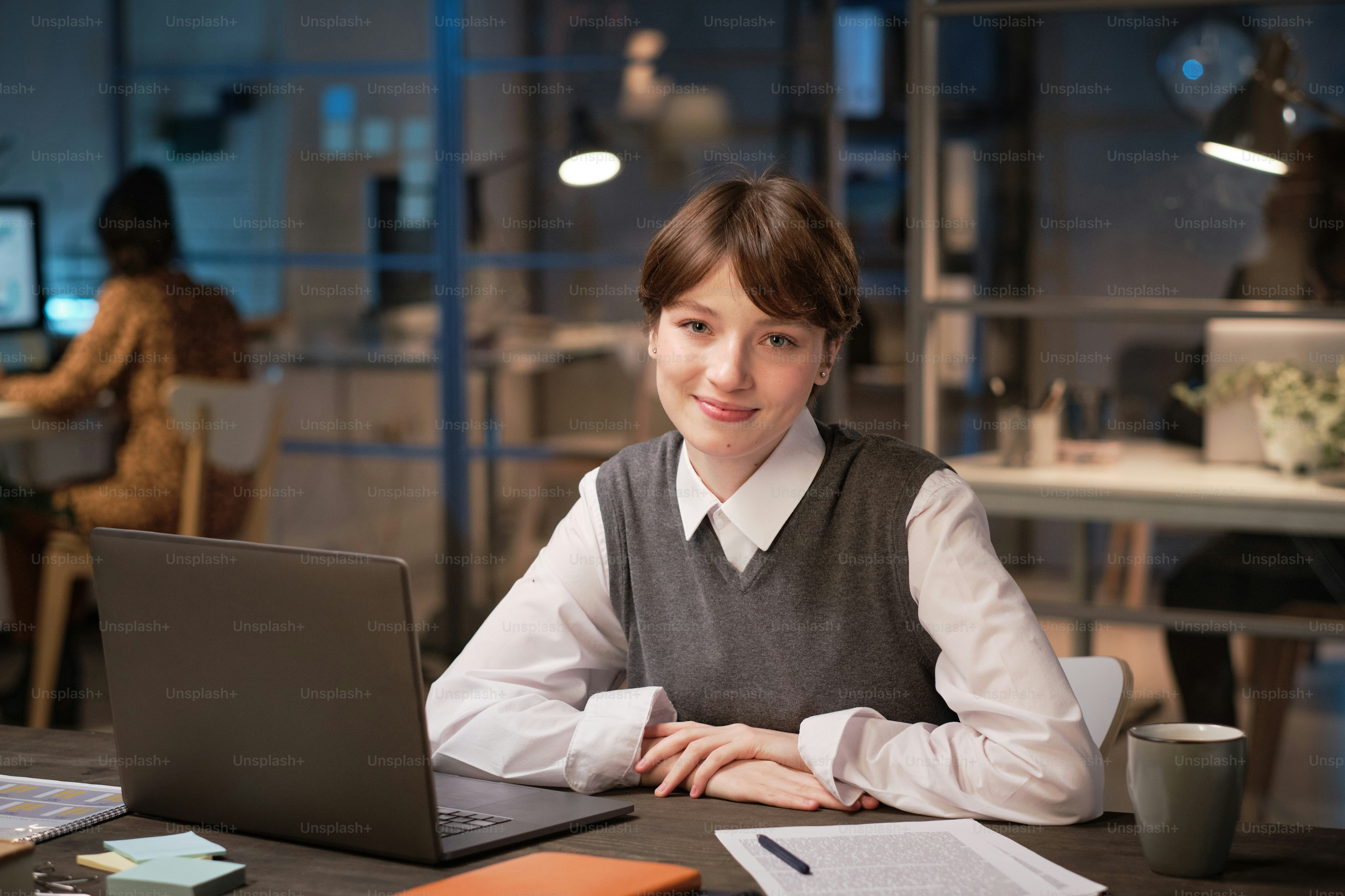 Portrait of young businesswoman sitting at the table with laptop and smiling at camera during her work at office