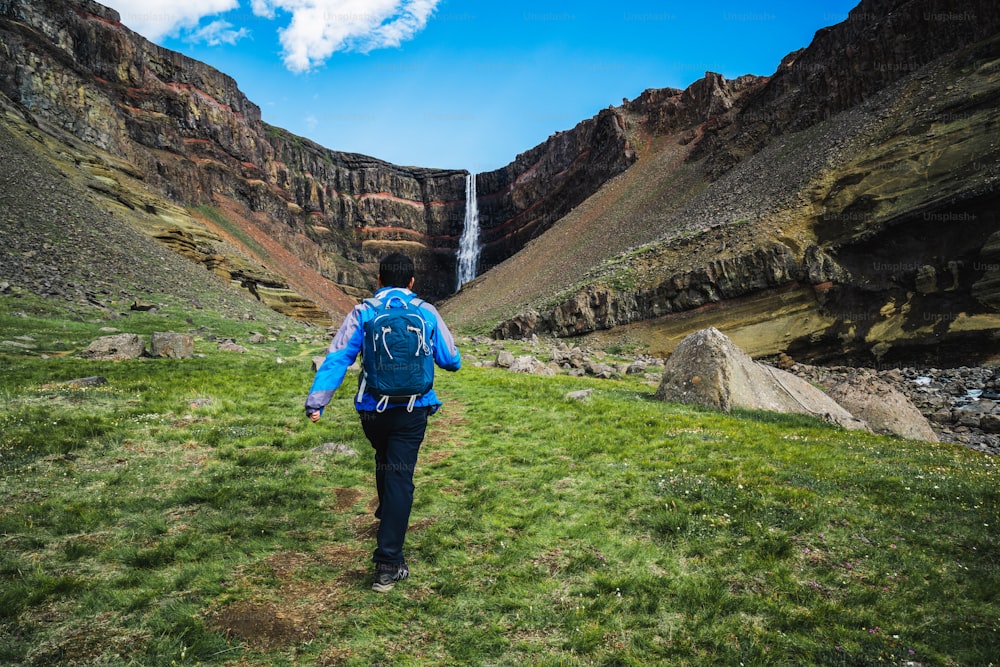 Viaggiatore dell'uomo che fa escursioni nel paesaggio estivo islandese alla cascata di Hengifoss in Islanda. La cascata si trova nella parte orientale dell'Islanda.
