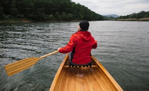 Rückansicht eines Mannes, der Kanu auf dem See paddelt. Regentag Bootsfahrt.