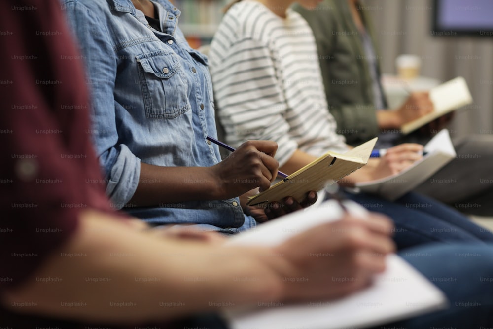 Close-up of people sitting and writing in notebooks during seminar at office