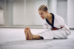 Female martial arts athlete with a disability warming up for taekwondo training in health club.