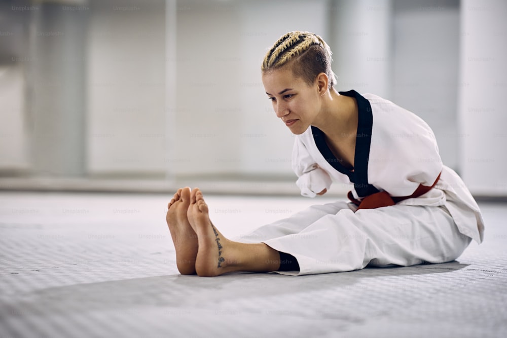 Atleta femenina de artes marciales con discapacidad calentando para el entrenamiento de taekwondo en un gimnasio.