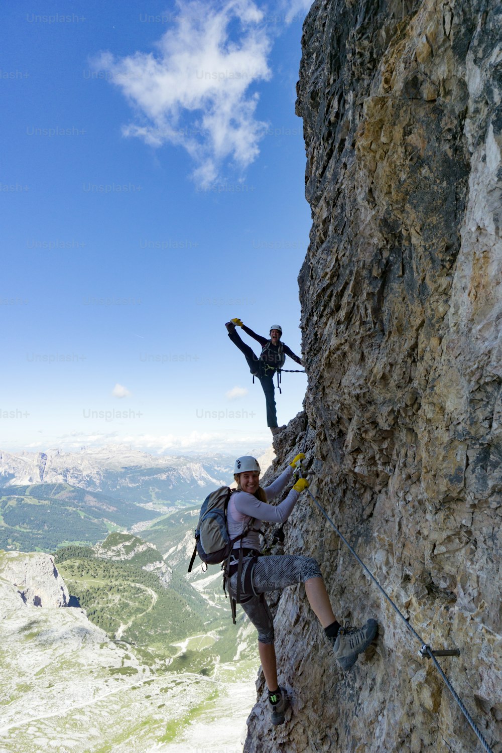 Vertical view of an attractive female climbers on a steep Via Ferrata in the Italian Dolomites with a great view behind and having fun