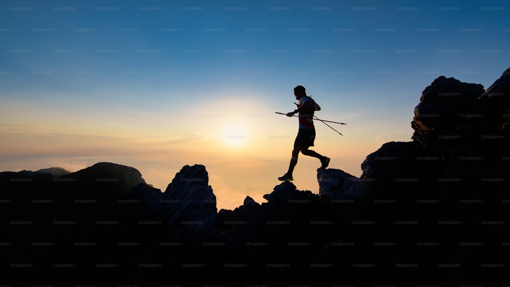 Sunset silhouette of skyrunner man descending from alpine ridge with poles