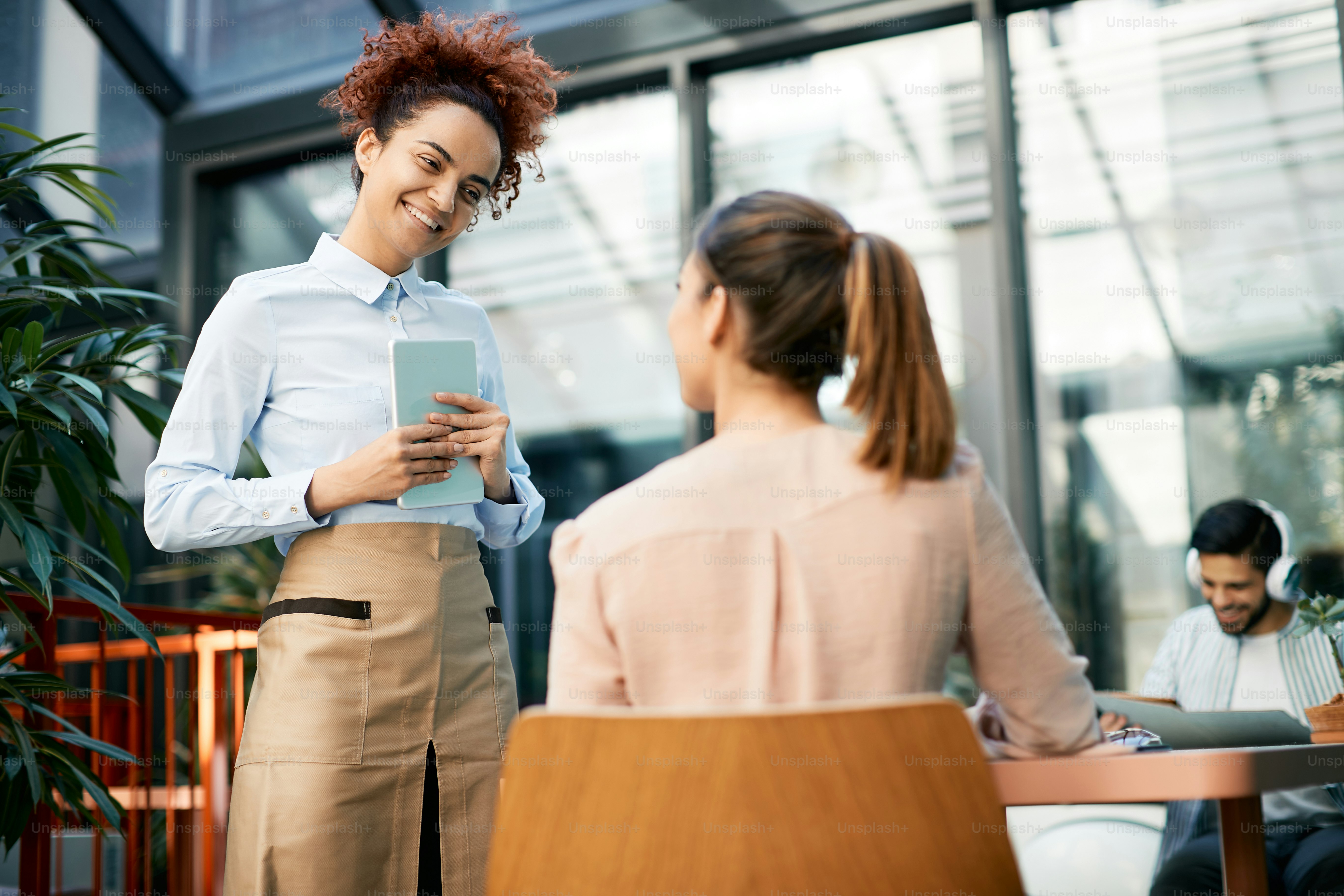 Happy waitress with digital tablet talking to a woman while taking order in a cafe.