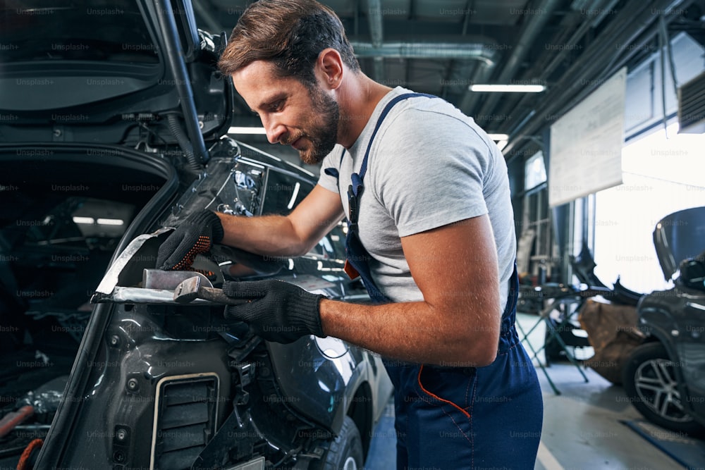 Peening of car part with hammer done by a mechanic in auto repair shop