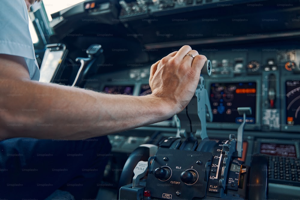 Foto recortada de un piloto profesional sentado en la cabina de vuelo empujando el acelerador de la aeronave hacia arriba