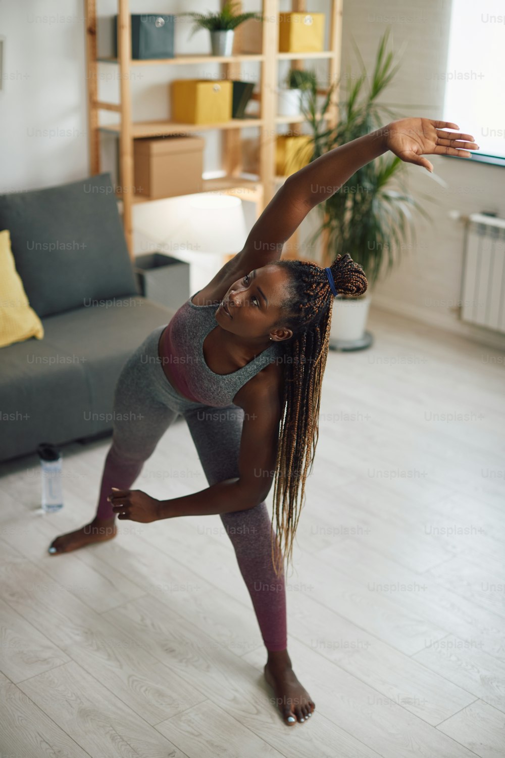 Young African American sportswoman warming up and stretching at home.