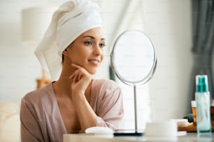 Young woman with pure and fresh face skin looking her self in a mirror at home.