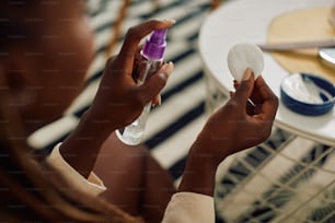 Primer plano de una mujer negra que usa un producto de belleza en una botella de spray mientras cuida la piel de su cara.