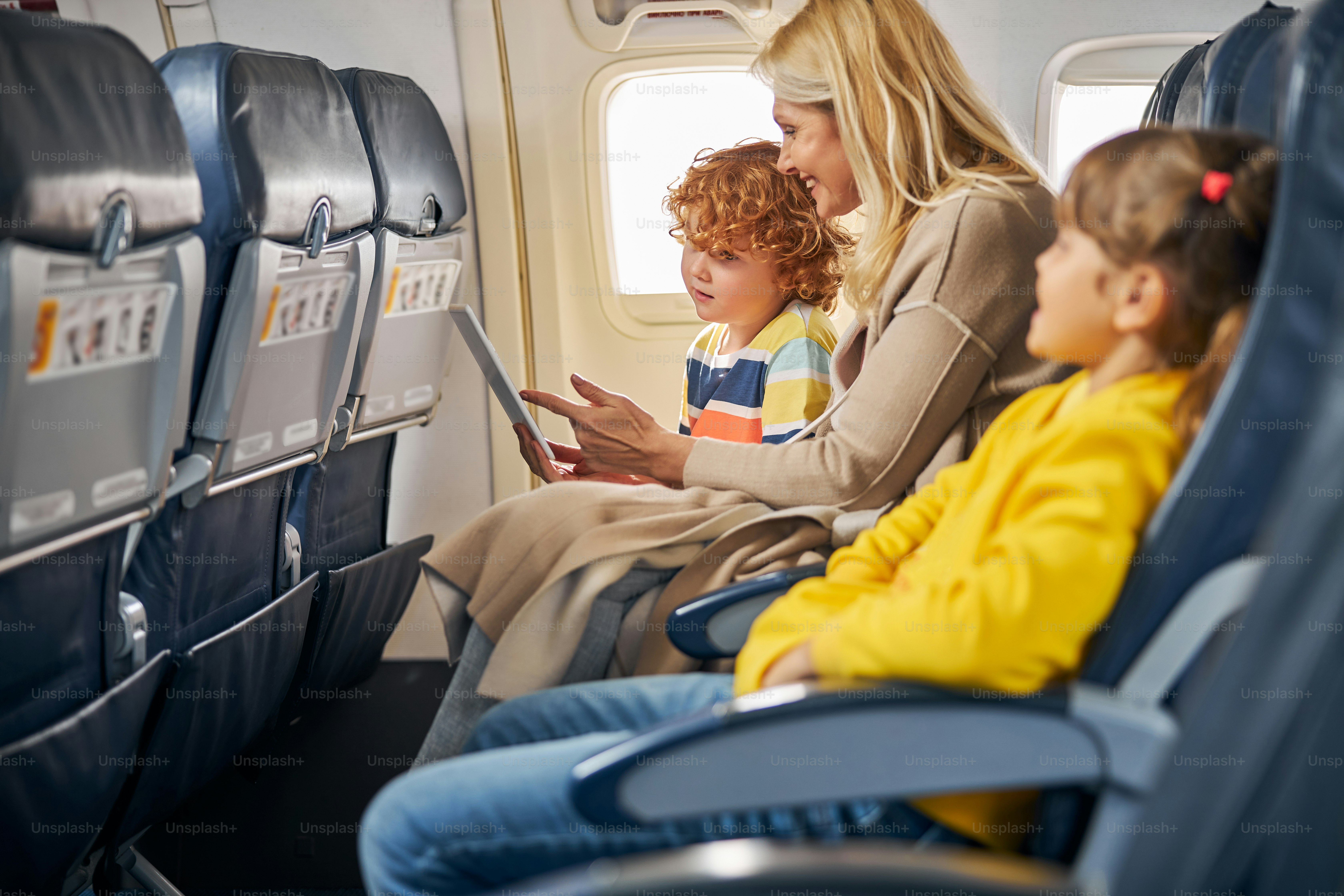 Joyful mother sitting near her son while pointing at a tablet screen and demonstrating some information