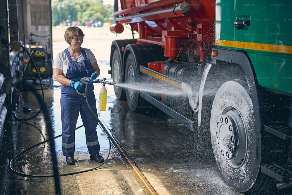 Cheerful female person wearing uniform while washing big special transport