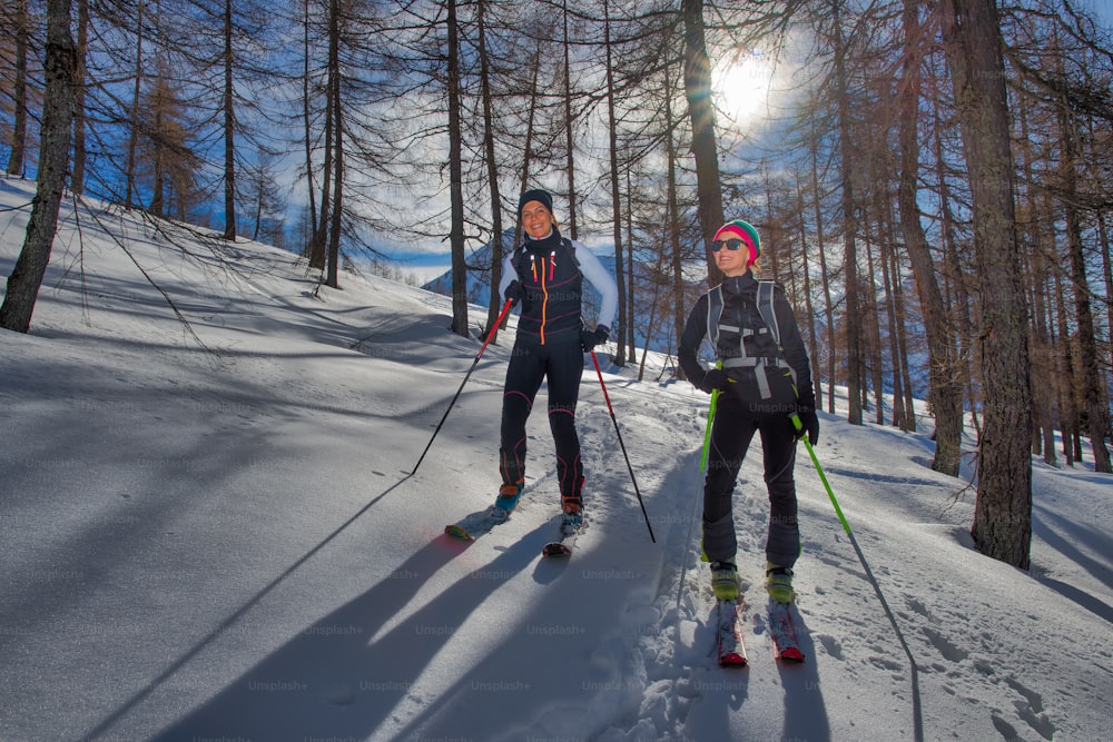 Dos chicas en el bosque con esquís de montaña ascienden.