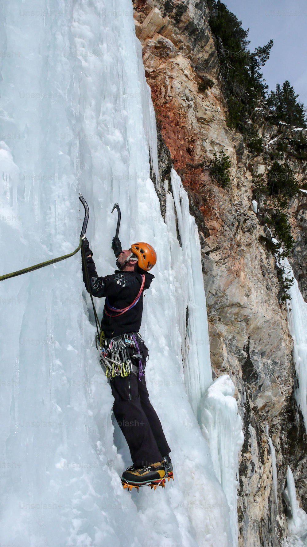 アヴェール渓谷のスイスアルプスの美しい冬の日に急な凍った滝の男性のアイスクライマー