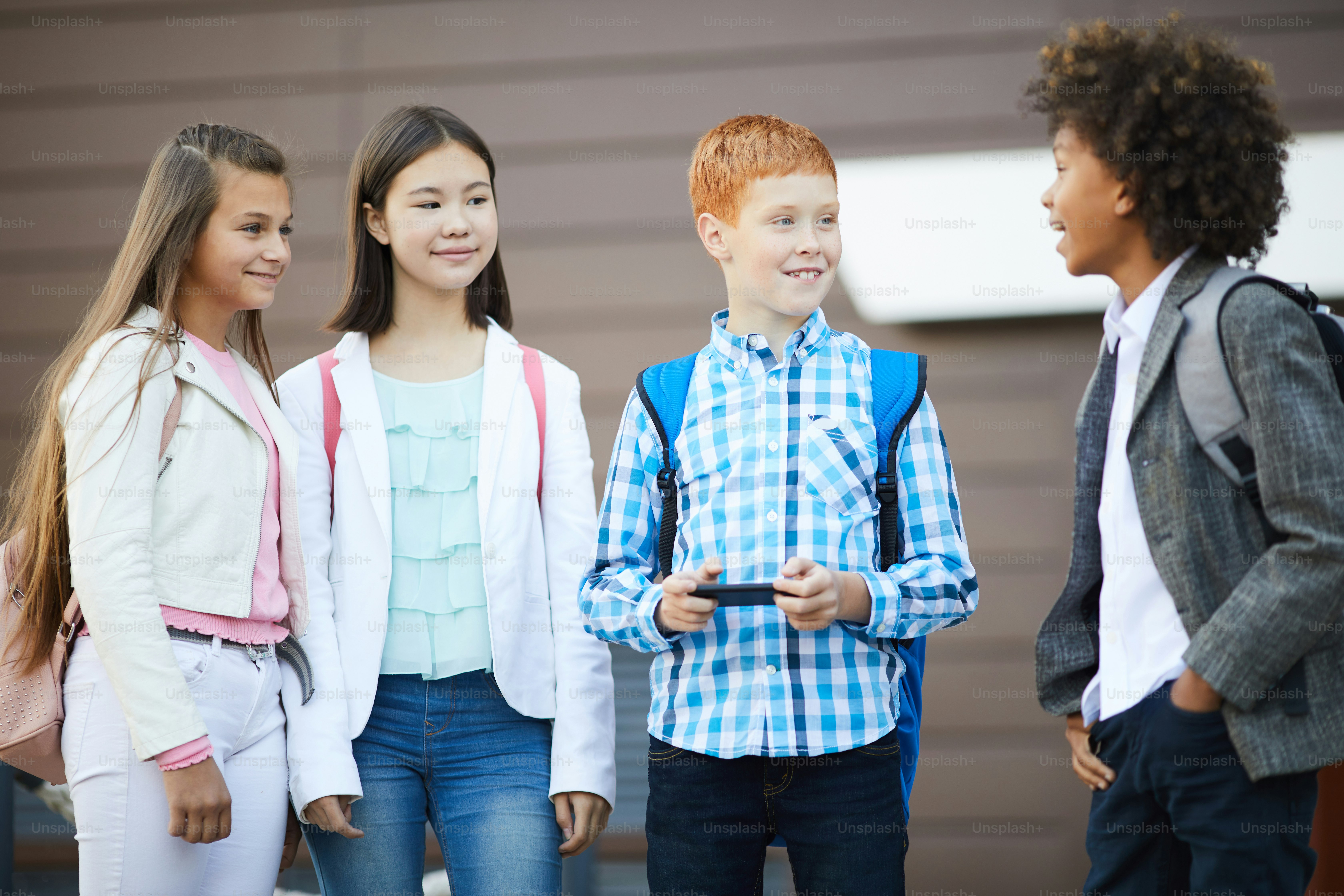 Grupo de crianças em idade escolar sorrindo e conversando com seu colega africano antes das aulas na escola