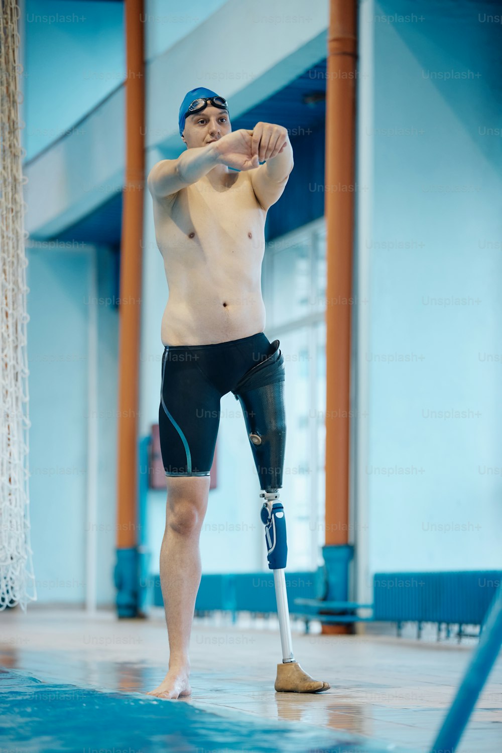 Schwimmer in voller Länge mit künstlichen Bein-Entspannungsübungen beim Aufwärmen für das Schwimmtraining im Hallenbad.