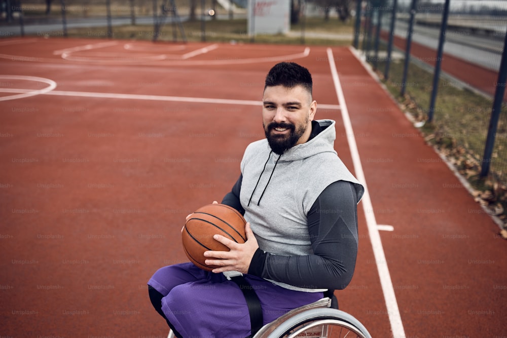 Atleta felice con disabilità che gioca a basket in carrozzina all'aperto e guarda la macchina fotografica. Copia spazio.