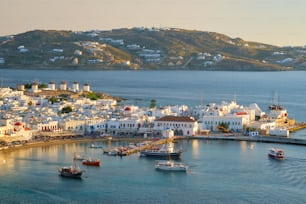 View of Mykonos town Greek tourist holiday vacation destination with famous windmills, and port with boats and yachtson sunset . Mykonos, Cyclades islands, Greece. With horizontal camera panning