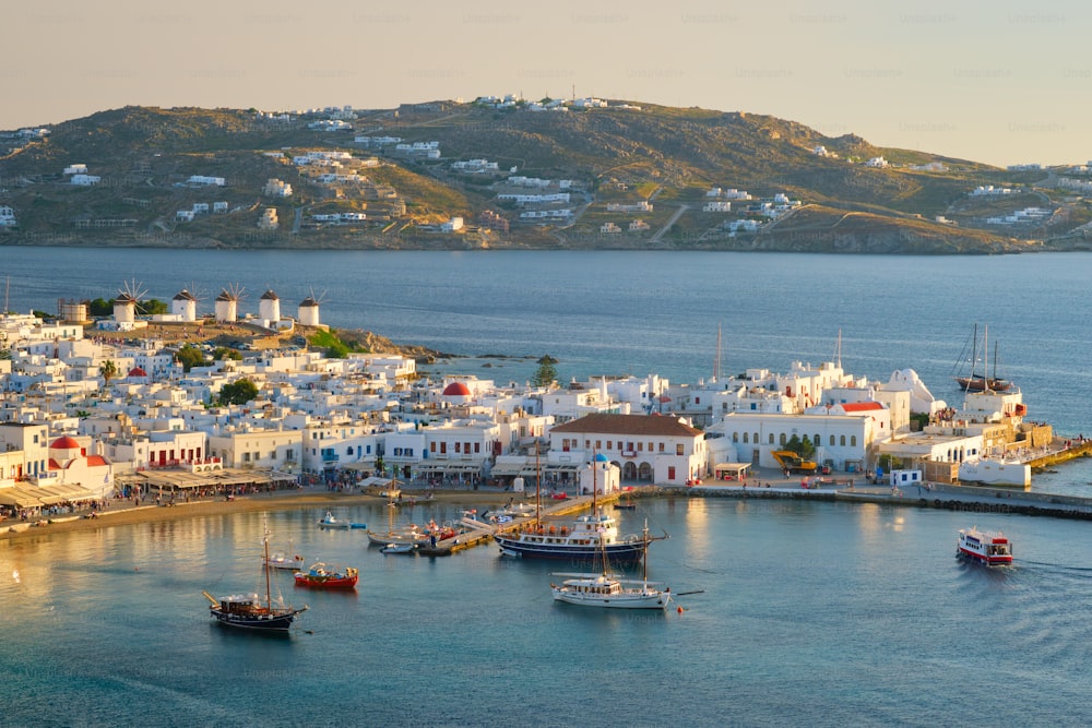 View of Mykonos town Greek tourist holiday vacation destination with famous windmills, and port with boats and yachtson sunset . Mykonos, Cyclades islands, Greece. With horizontal camera panning