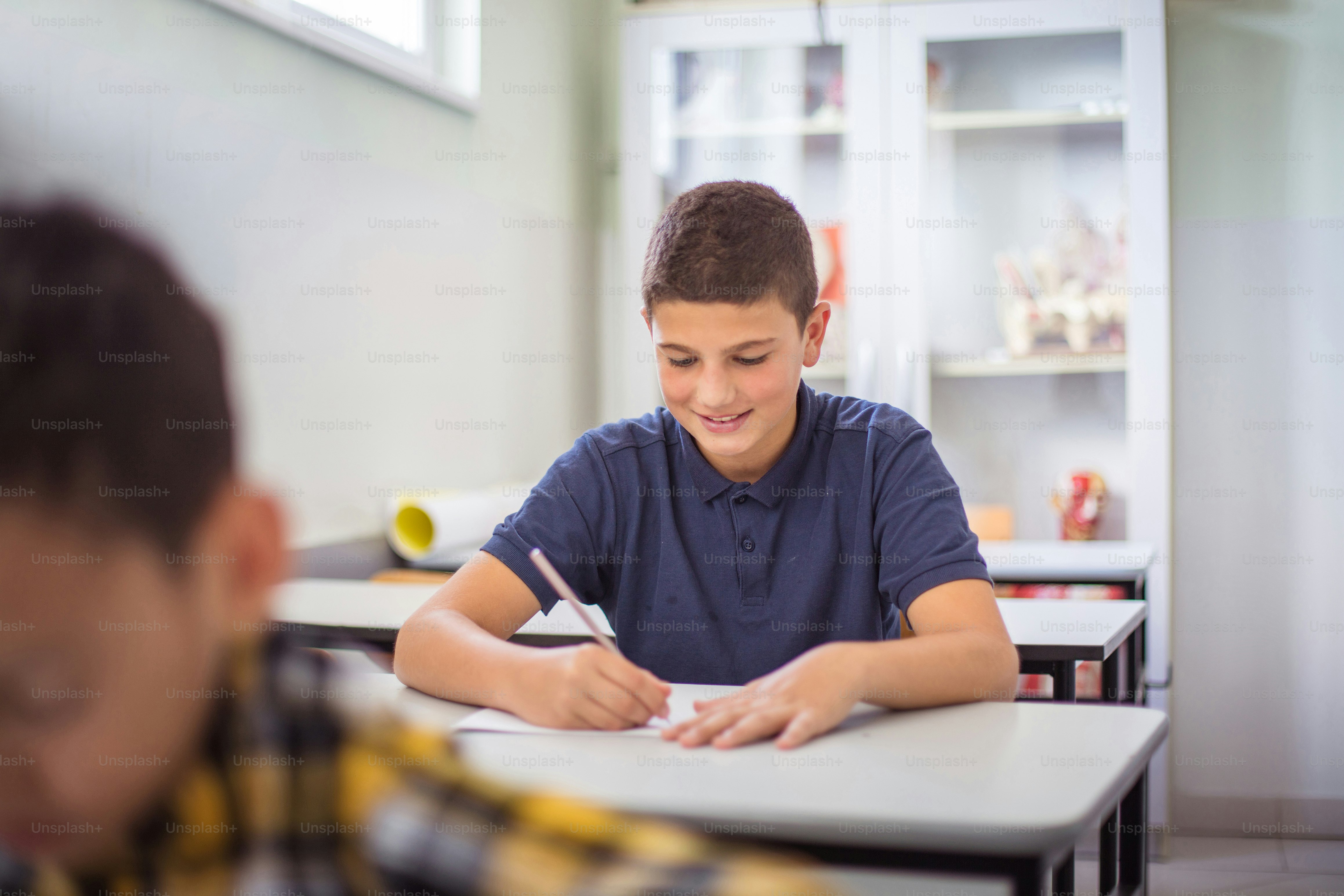 Two boys working education exam in classroom.  Teenagers students sitting in the classroom.  Focus is on background.