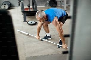 Mature sportsman exercising with barbell during strength training in gym.