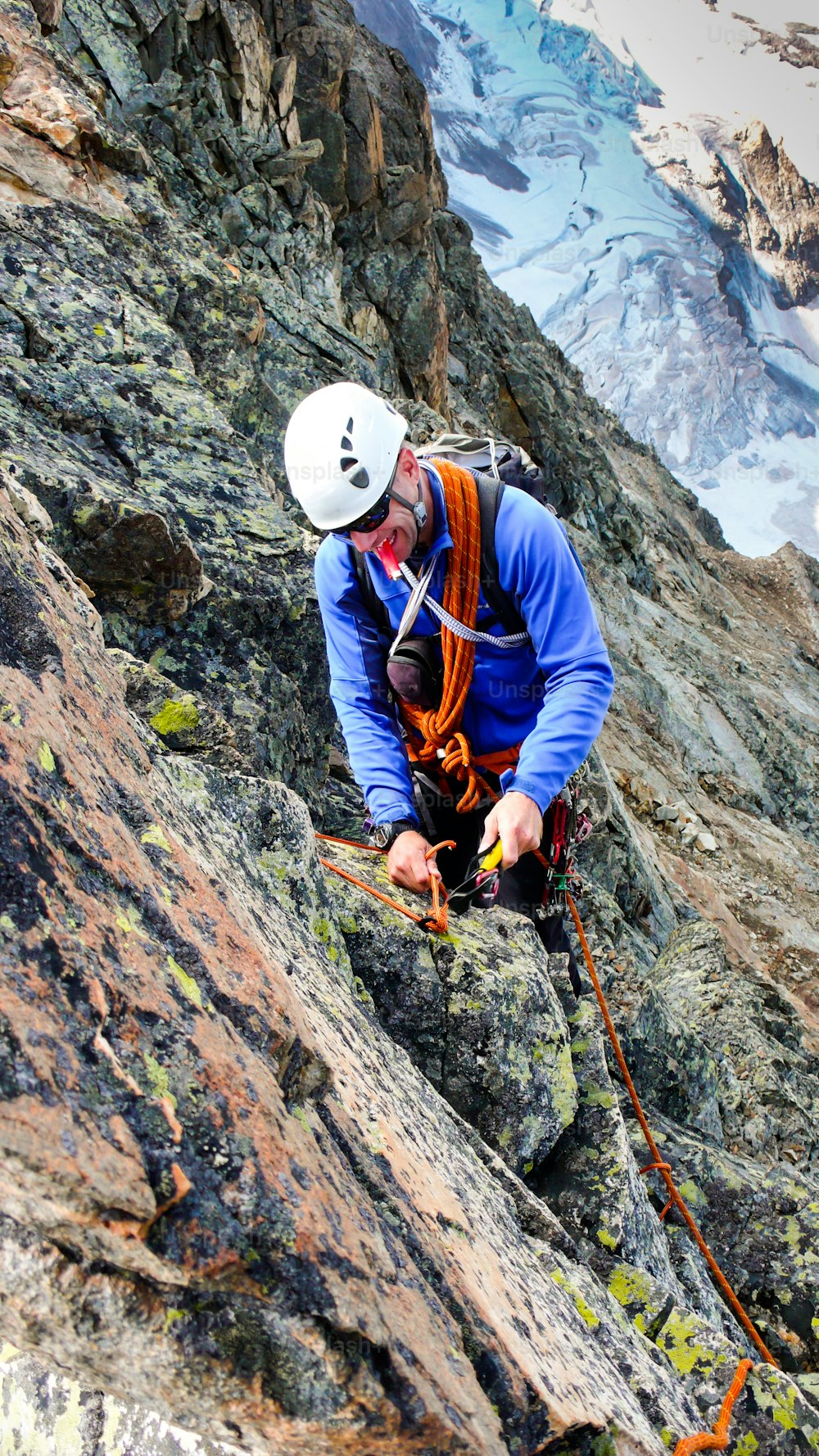 A male mountain guide building a traditional belay stance with pitons to rappel from a high alpine peak