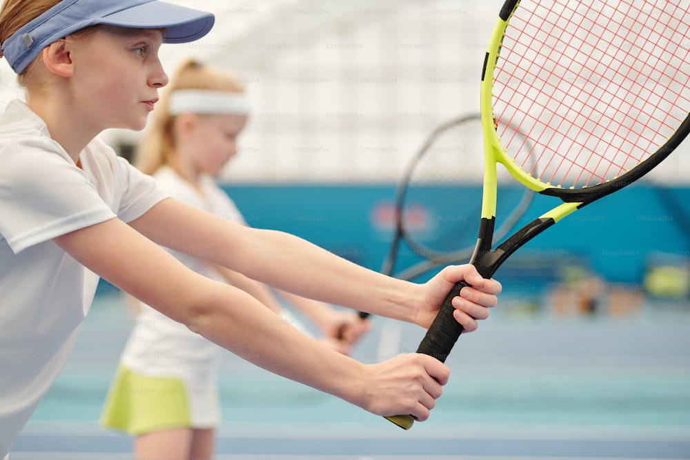 Adolescente seria y concentrada en ropa deportiva de pie en el estadio y sosteniendo una raqueta de tenis lista para empujar la pelota durante el juego