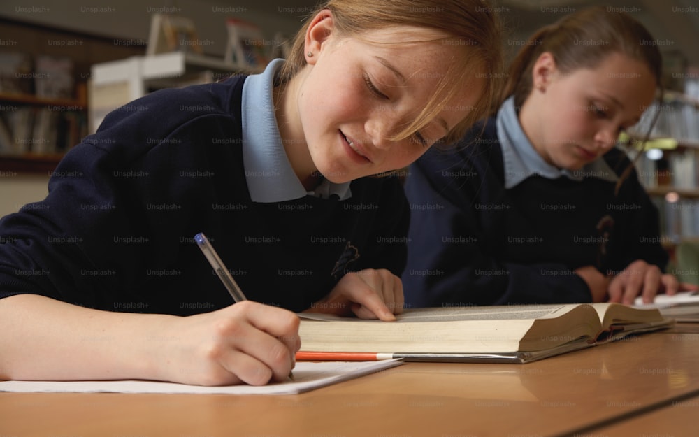 Schoolgirl (11-13) making notes from book in library, smiling