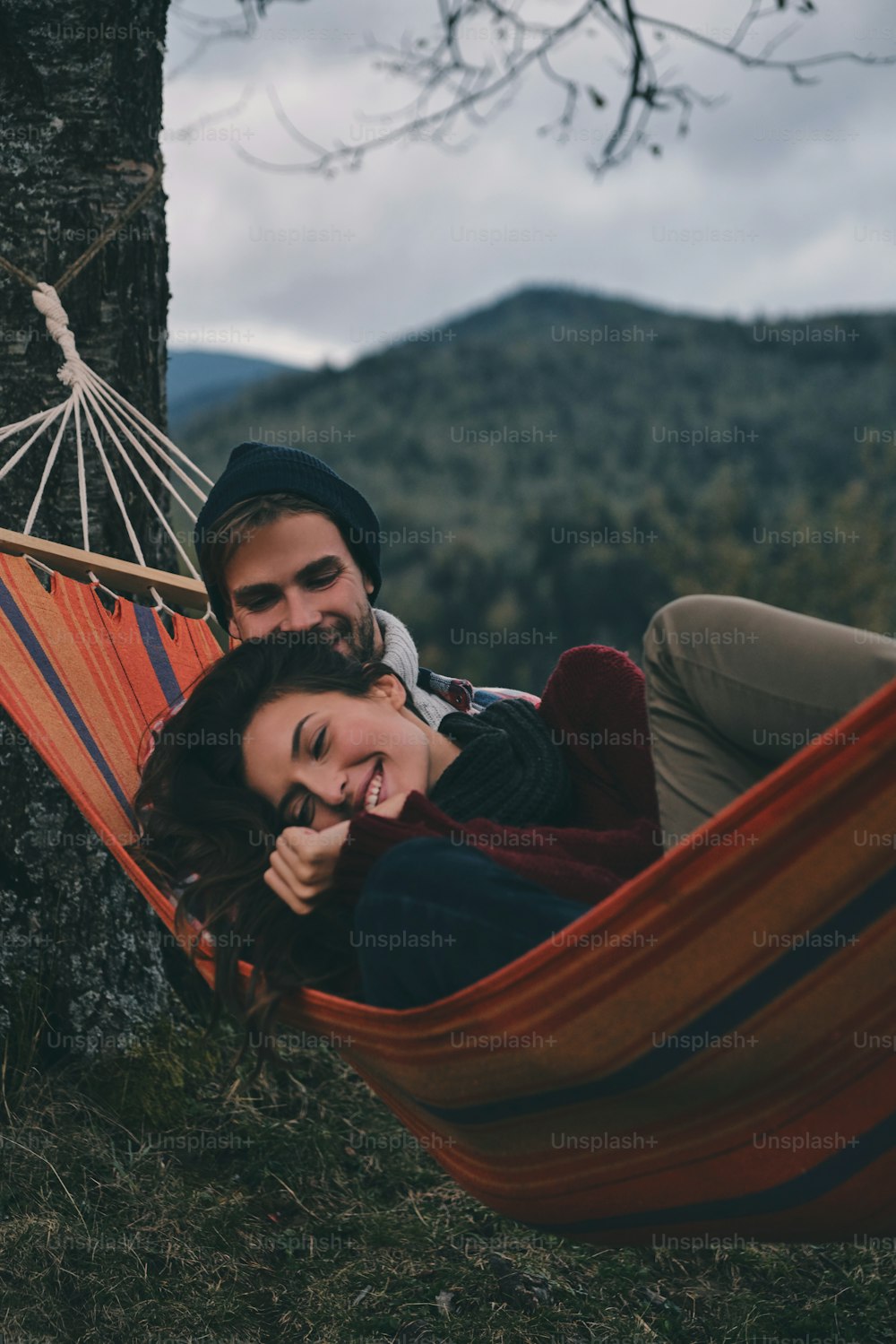 Beautiful young couple embracing and smiling while lying in hammock under the tree
