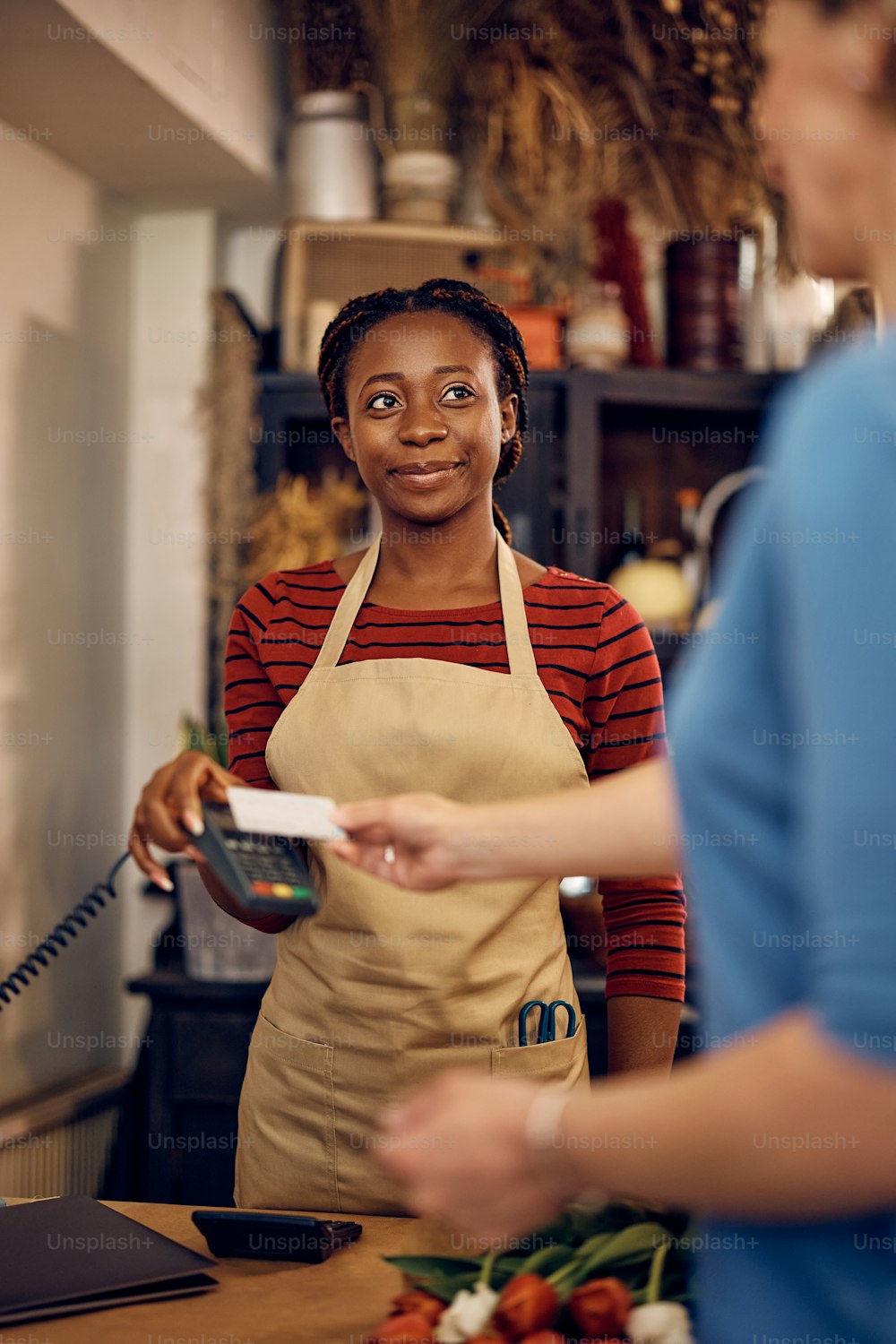 Femme afro-américaine heureuse travaillant comme fleuriste et recevant le paiement par carte de crédit de son client dans un magasin de fleurs.