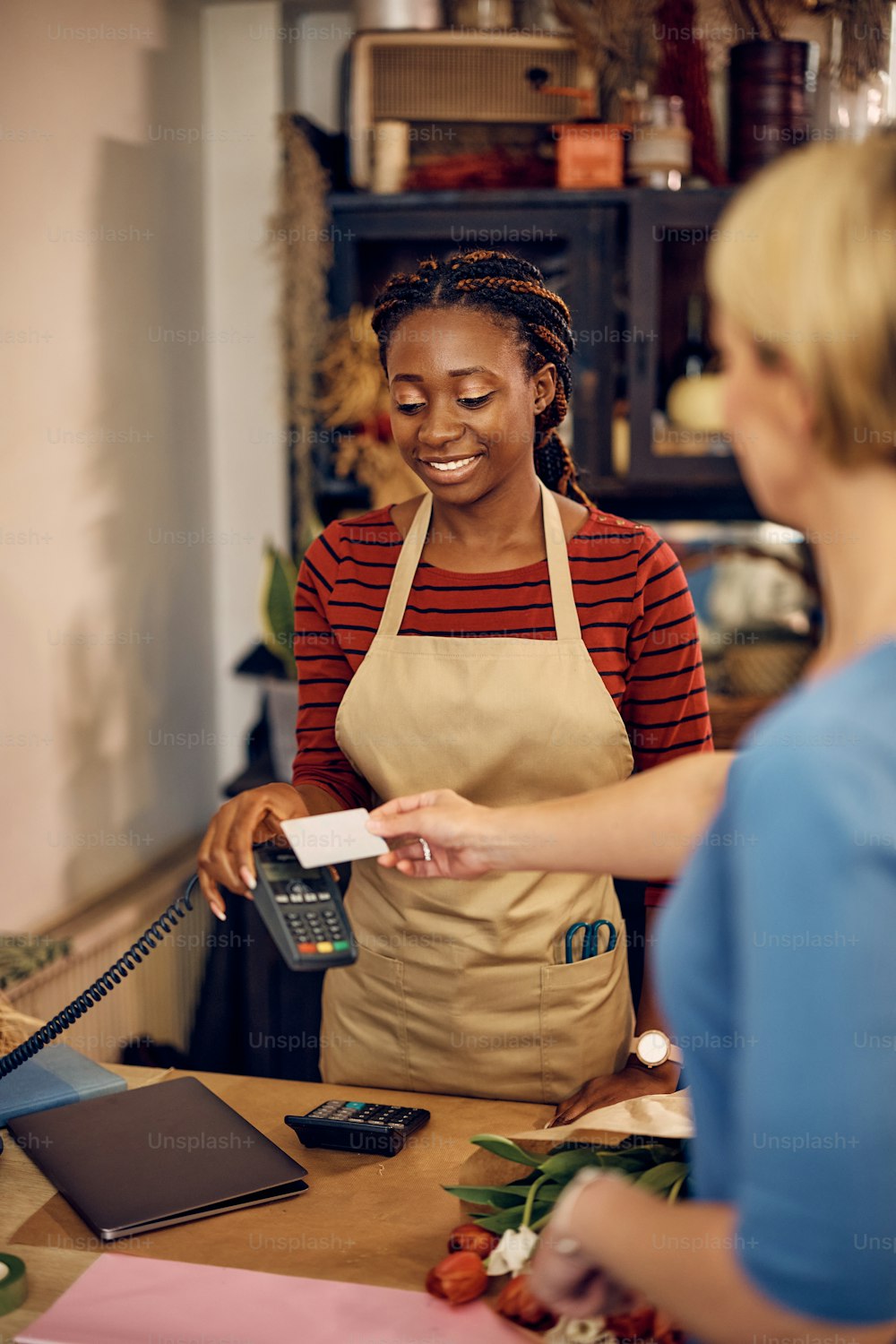 Happy African American flower shop owner accepting customer's credit card for a payment.