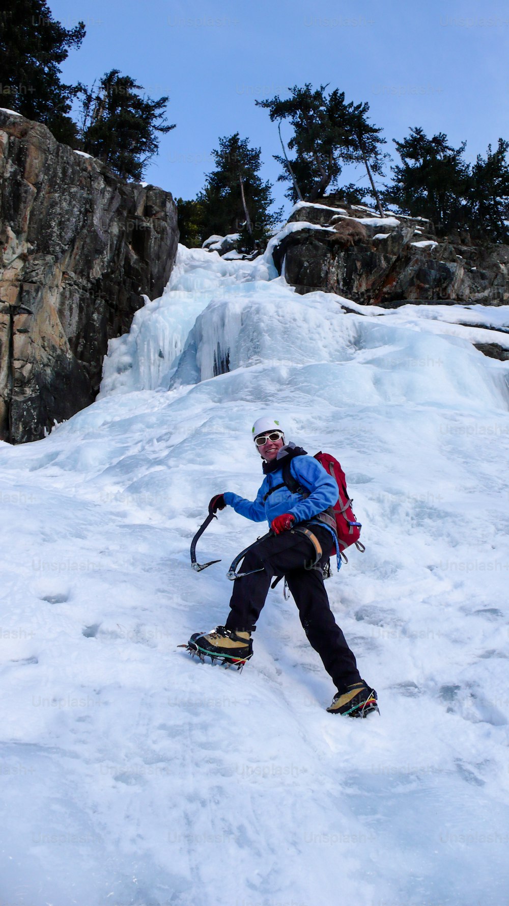 スイスの真冬のアルプスでゴージャスな凍った滝を登る青いジャケットを着た男性のアイスクライマー