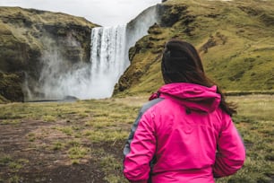 여름에 아이슬란드 시골의 장엄한 스코가포스 폭포의 아름다운 풍경을 감상하는 여성 여행자. 스코가포스는 아이슬란드와 유럽의 가장 유명한 자연 랜드마크이자 관광 명소입니다.