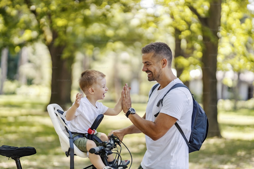 Happy parenting and raising a child. A boy sits in a bicycle basket and throws five dads standing next to him and holding bicycles. Smile and priceless family moments together during the summer days