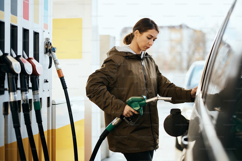 Mujer joven repostando el tanque de gasolina de su automóvil en una estación de servicio.