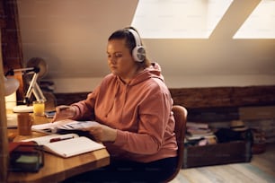 Female college student learning from a book while studying at home.